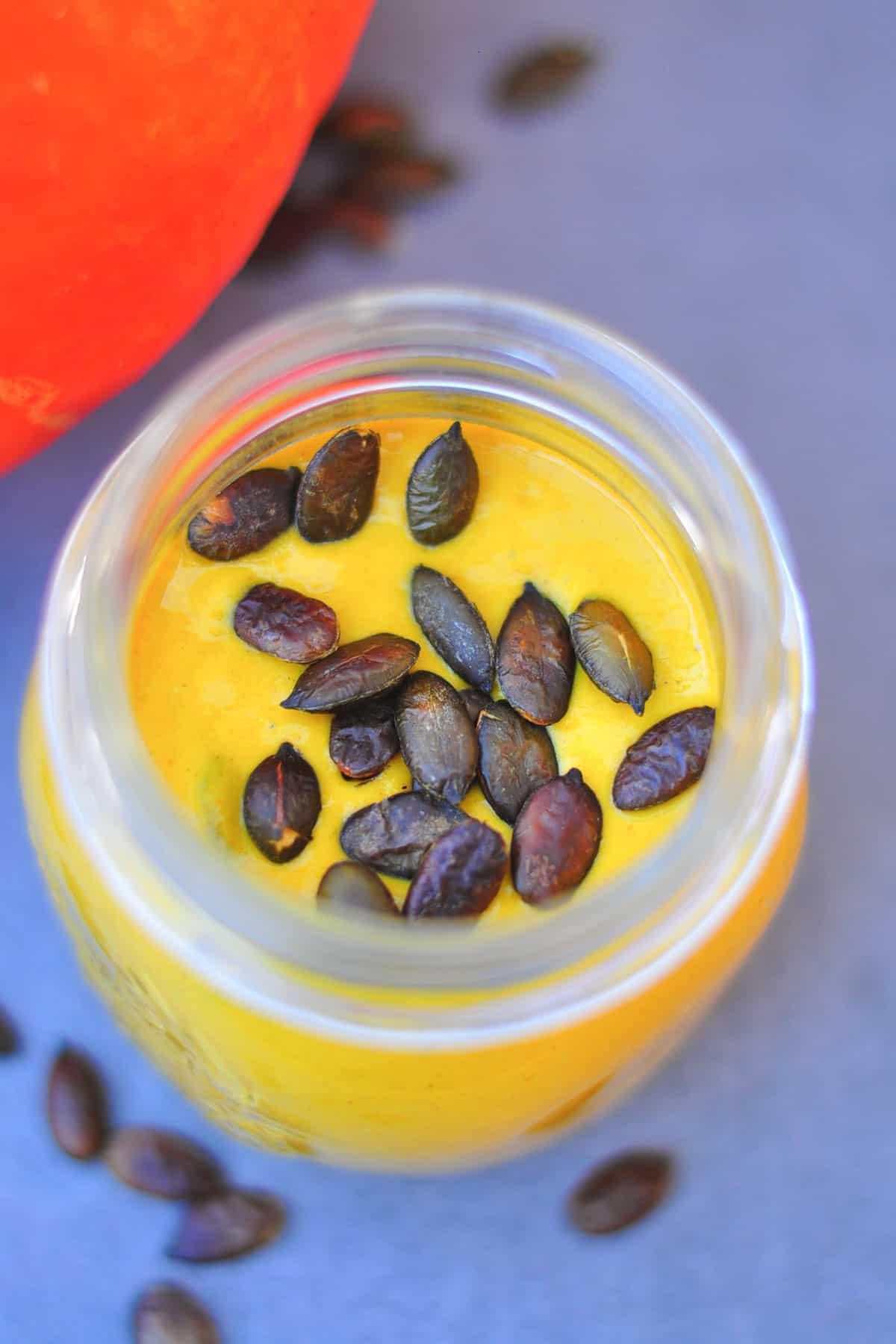 Mason Jar with yellow pumpkin smoothie in it topped with roasted pumpkin seeds