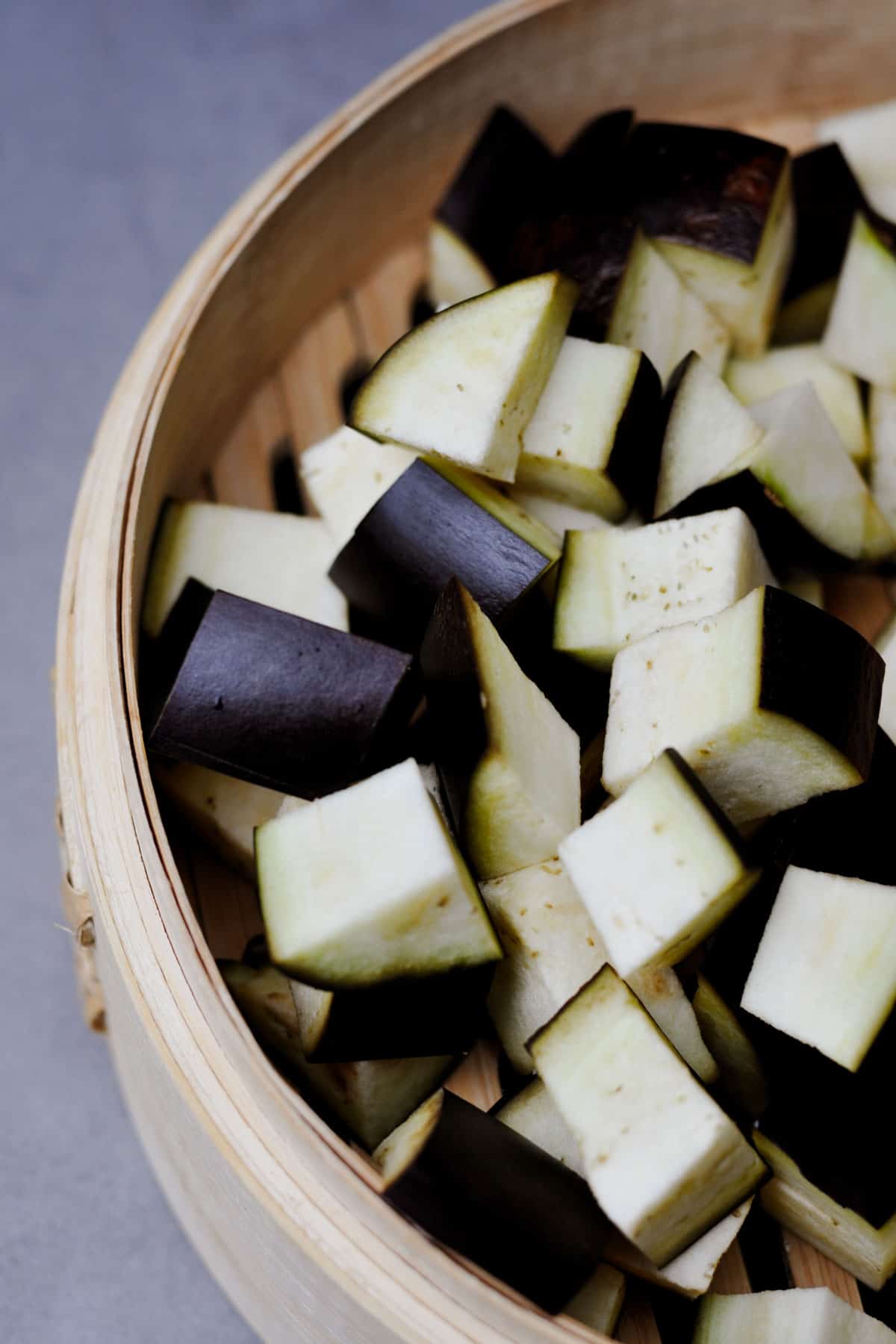 Freshly cut aubergine (eggplant) in cubes in a bamboo steamer