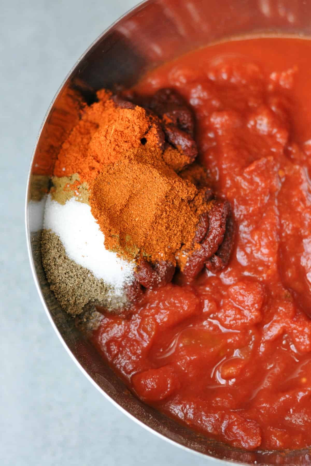 Chopped tomatoes in a metallic bowl with spices for vegan chili recipe