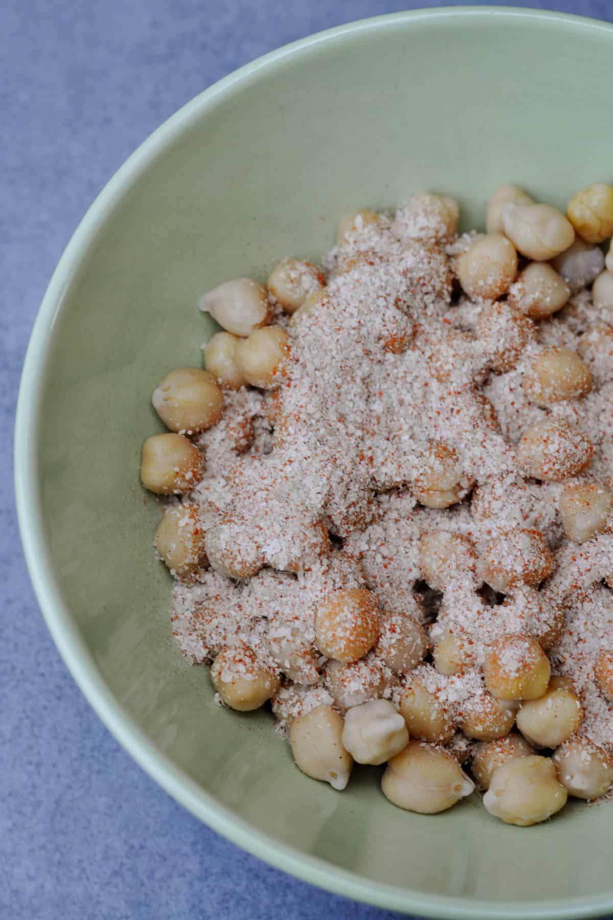 Cooked chickpeas with spices mix of nutritional yeast, chili powder and salt in a bowl