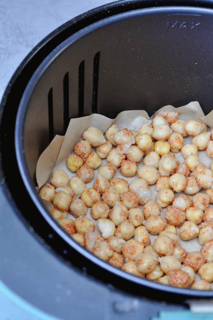 Cooked chickpeas with spices mix of nutritional yeast, chili powder and salt in an air fryer basket