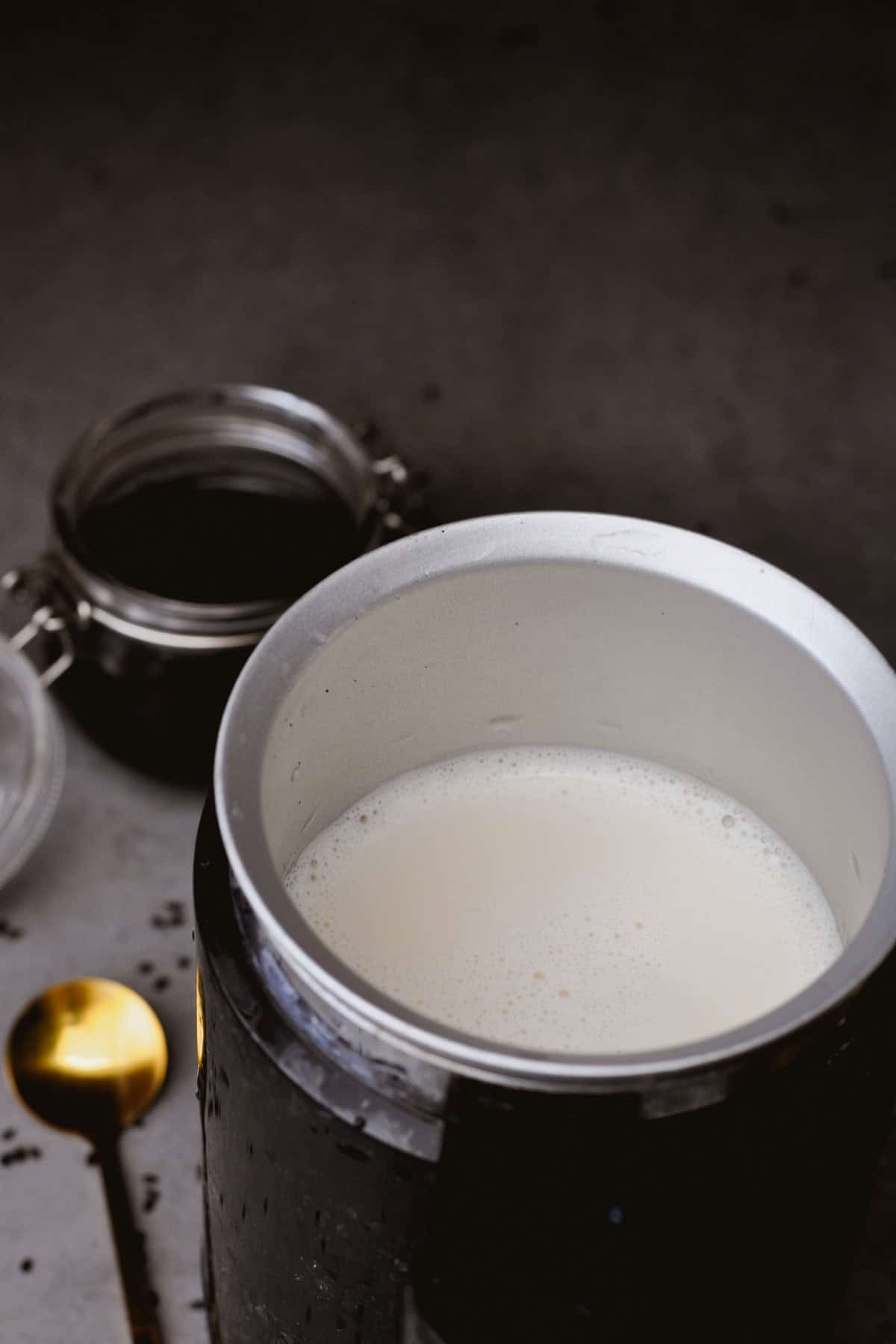 vegan milk in a milk frother and a small jar with black sesame paste