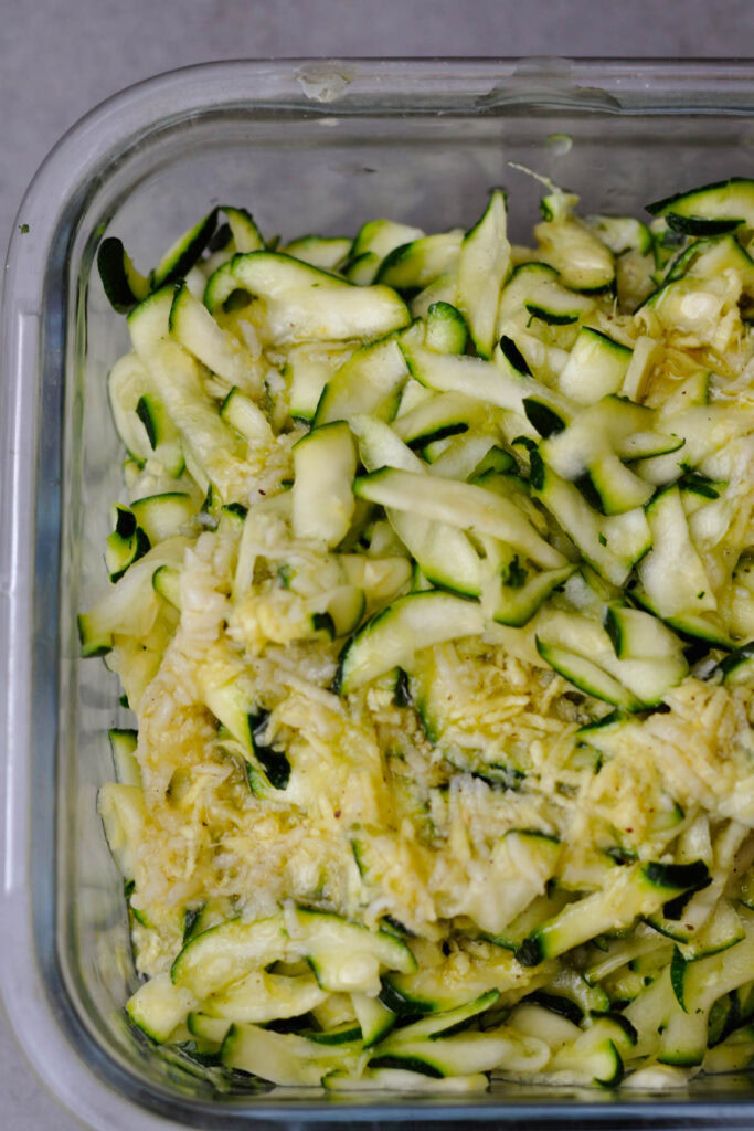 salted shredded zucchini in a glass container with vinaigrette