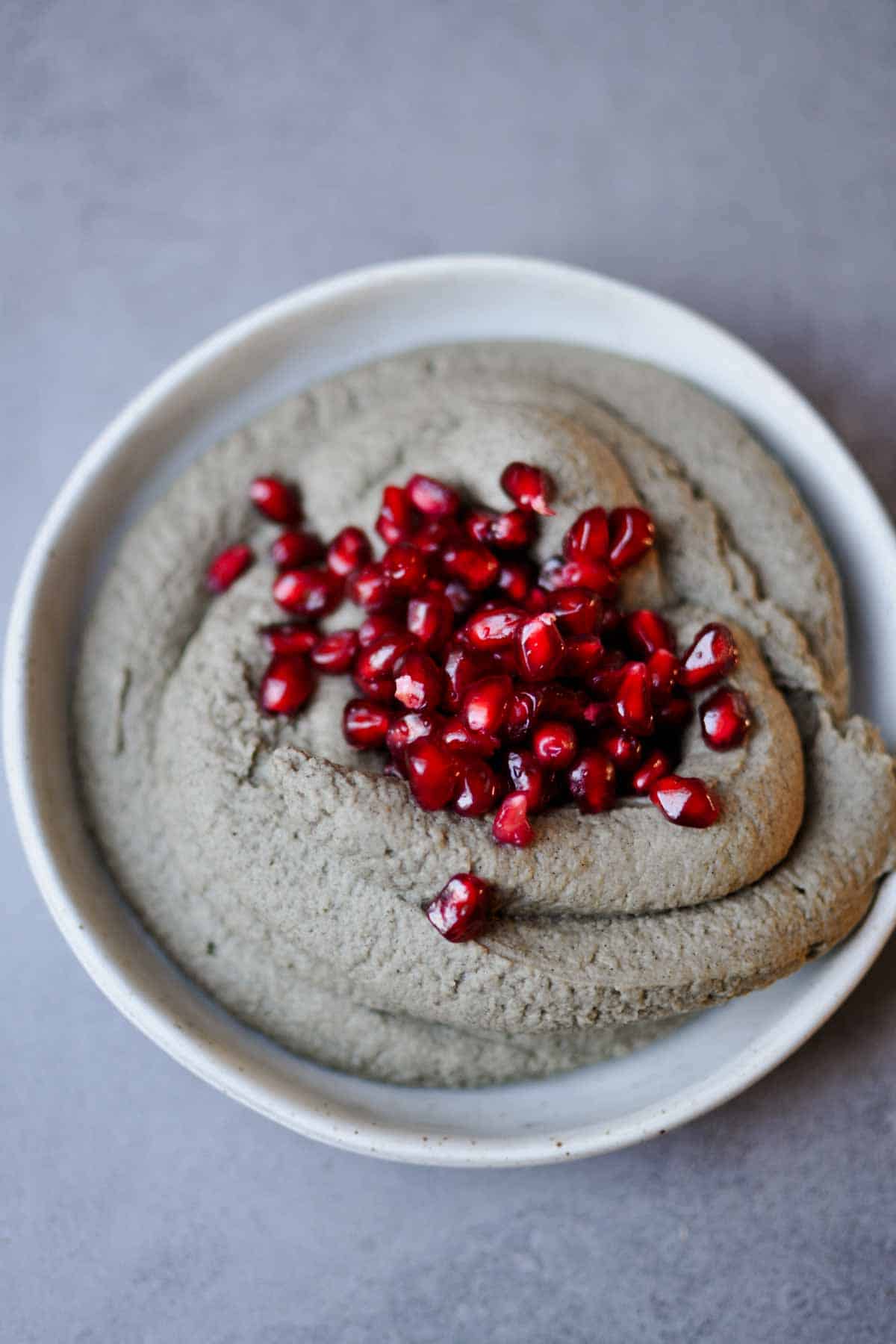 black sesame paste hummus on a plate topped with pomegranate seeds.