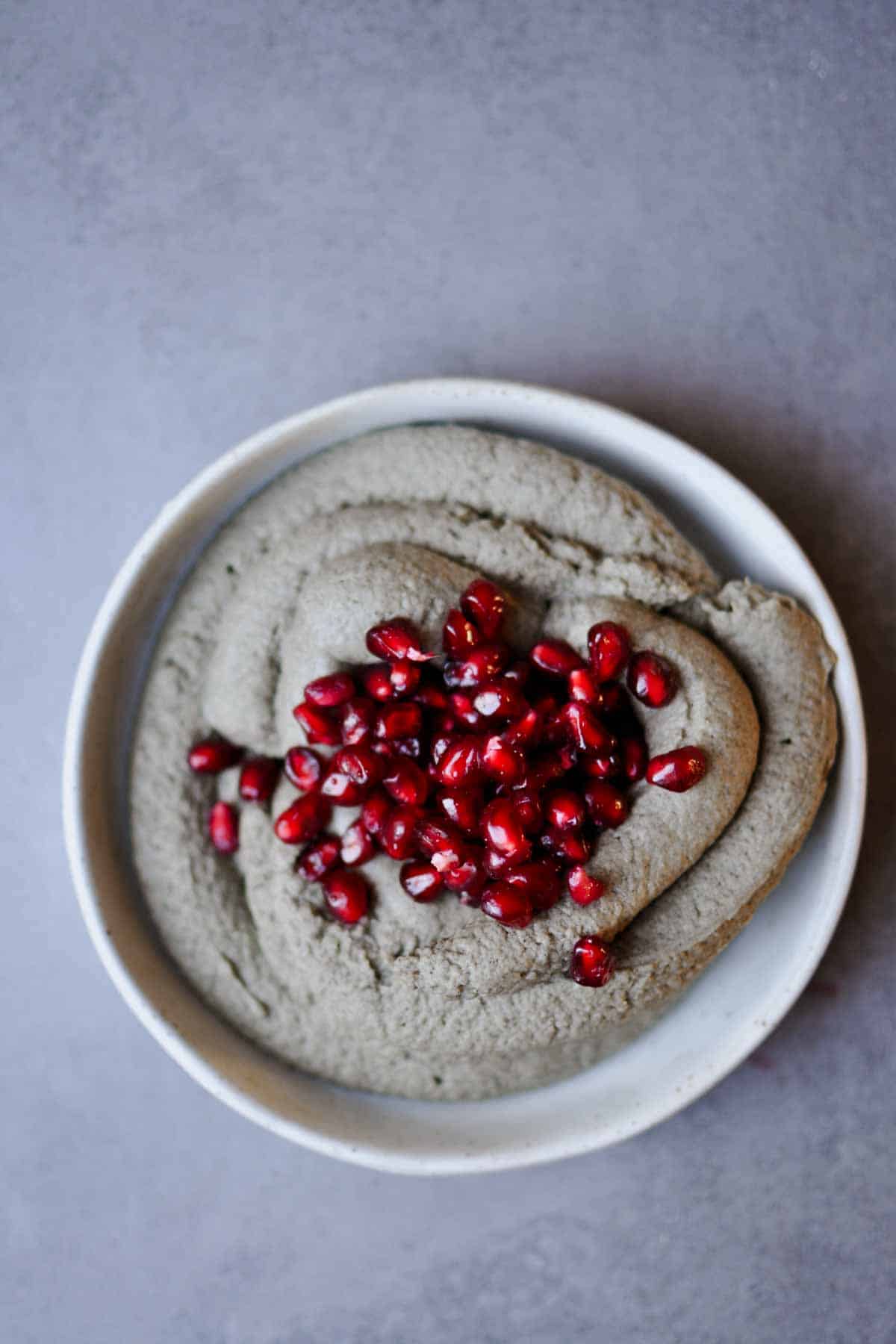 black sesame paste hummus on a white plate with pomegranate seeds topping