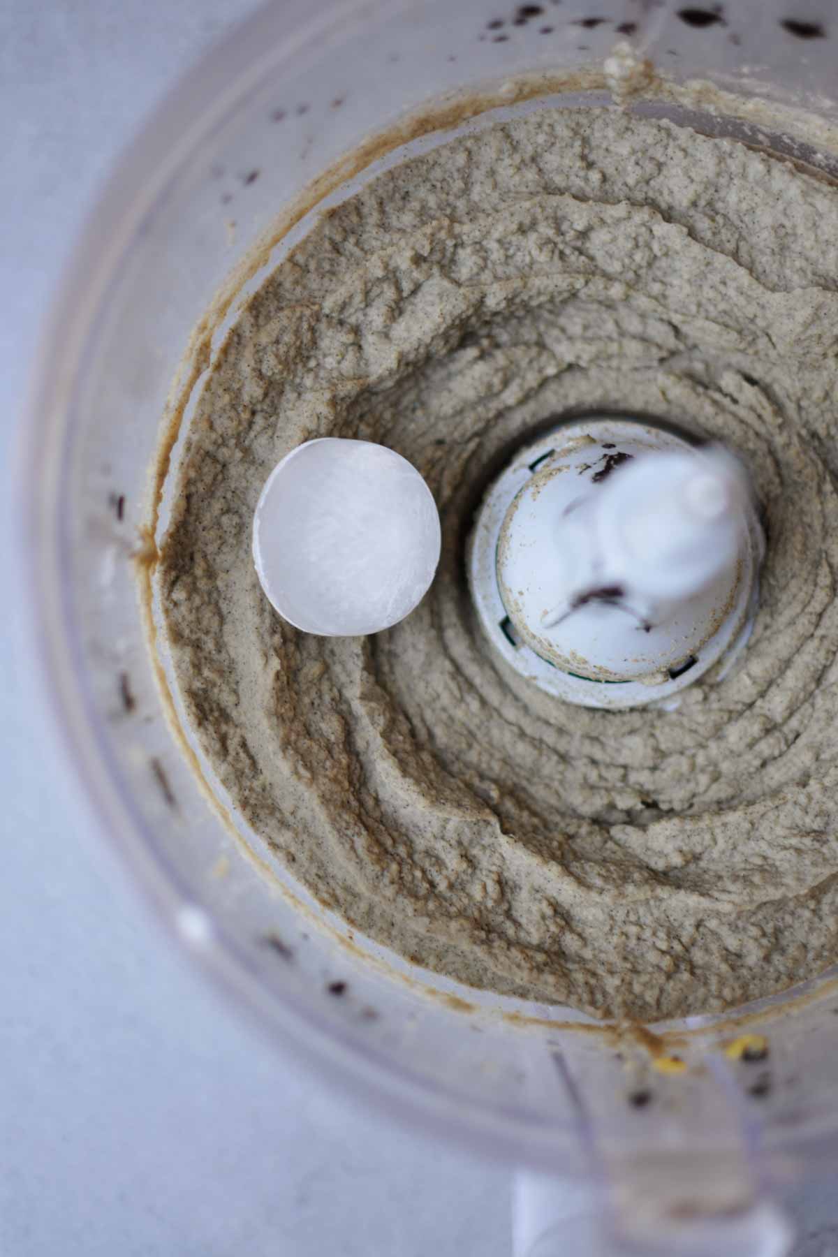 black sesame hummus mixed in a food processor with a cube of ice.