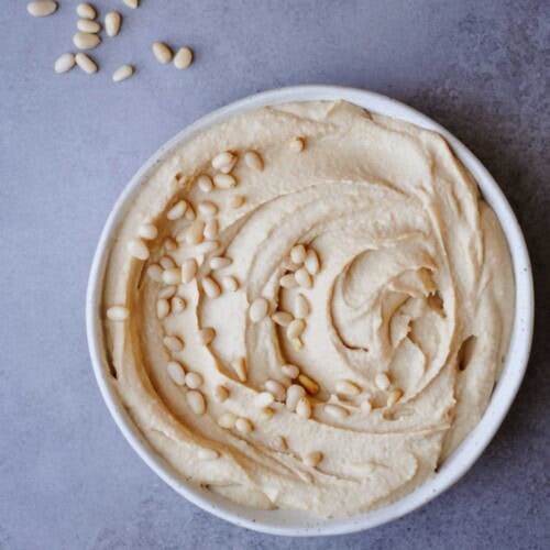 simple roasted pine nut butter hummus recipe (without tahini) in a white plate on a gray table.