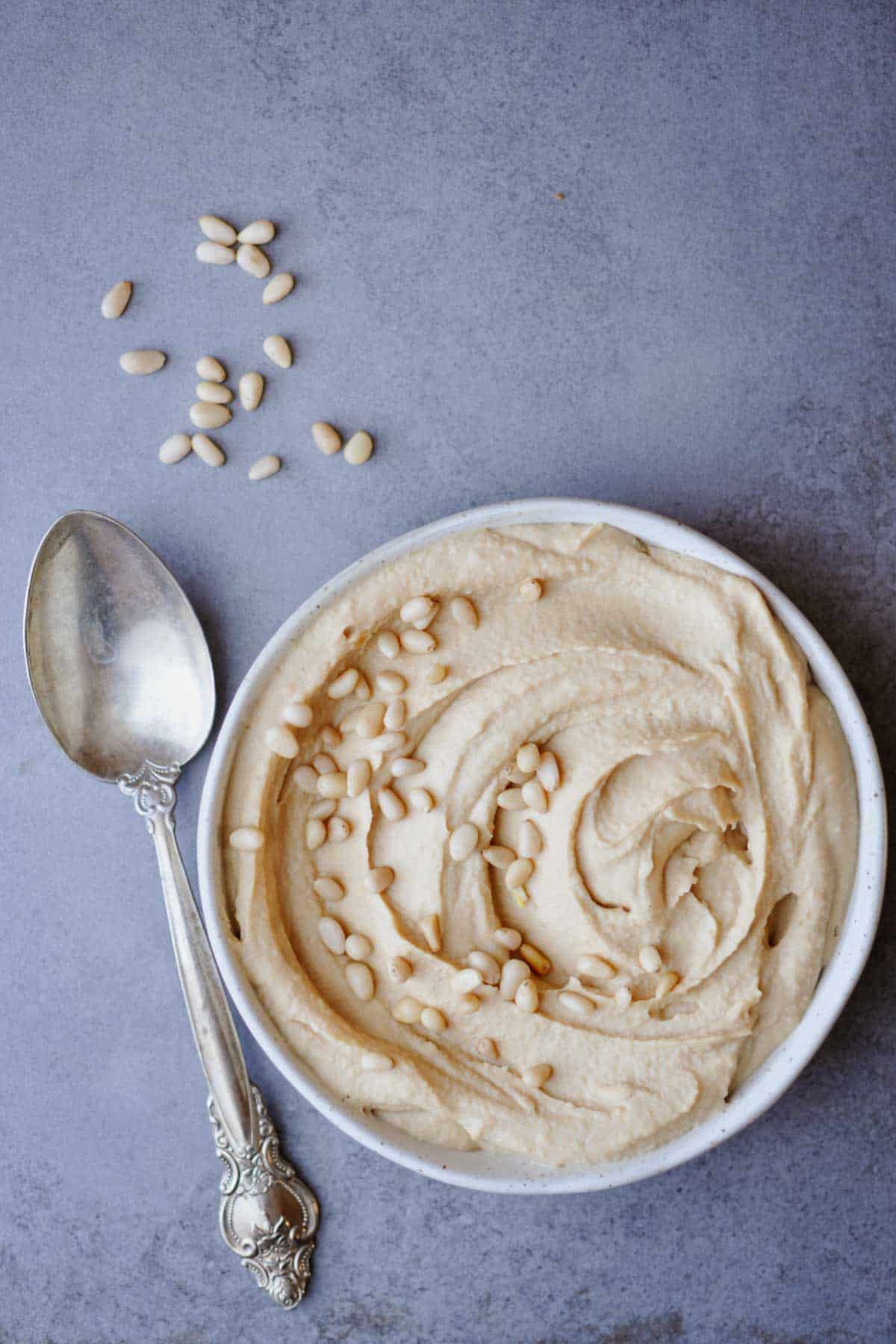 simple roasted pine nut butter hummus recipe in a white plate on a gray table.