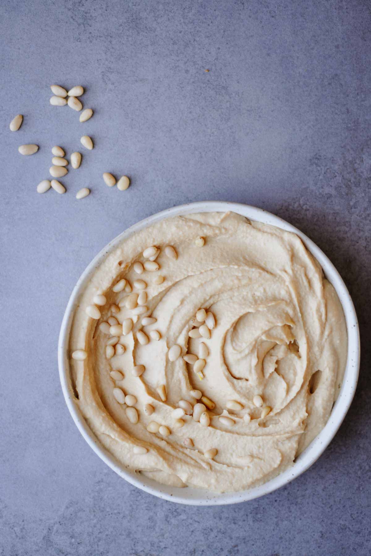 simple roasted pine nut butter hummus recipe (without tahini) in a white plate on a gray table.