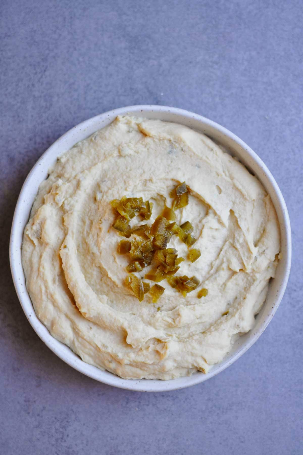 spicy jalapeno hummus with pickled jalapeno in a white plate.