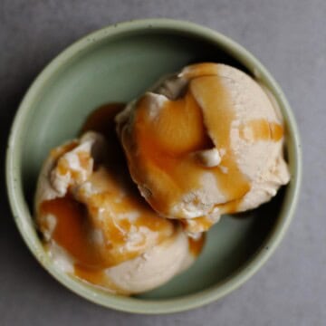 Bowl of vegan salted caramel ice cream on a grey table, showing its creamy texture and rich caramel color.